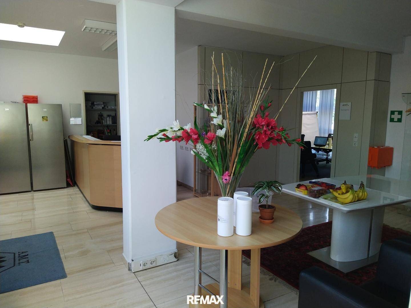 Empfangsbereich mit Holztresen, Blumenarrangement und Sitzgelegenheiten in einem Bürogebäude.