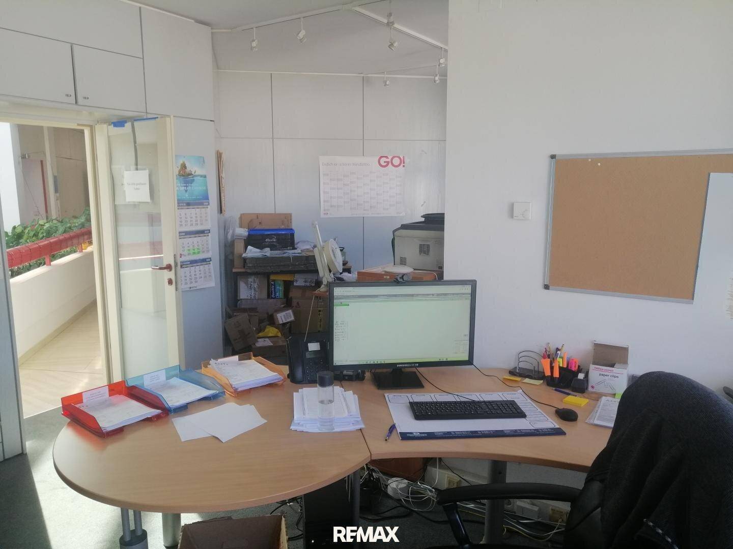 Büroraum mit einem runden Schreibtisch, Computer und Blick auf einen Flur mit Geländer.