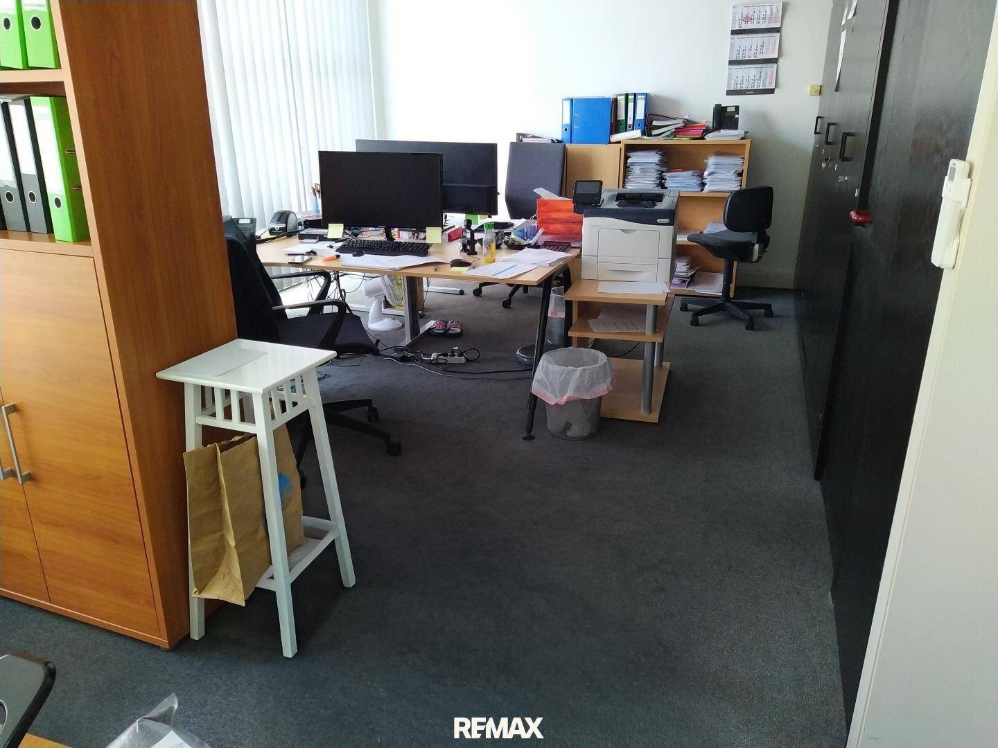 Großes Büro mit mehreren Arbeitsplätzen, Aktenschränken und Teppichboden.