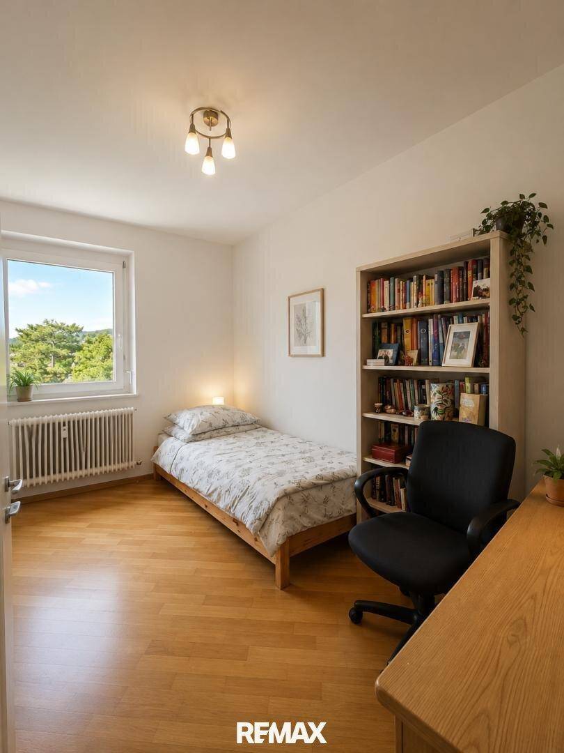 Helles Schlafzimmer mit Einzelbett, Schreibtisch und Bücherregal, bietet einen grünen Ausblick.