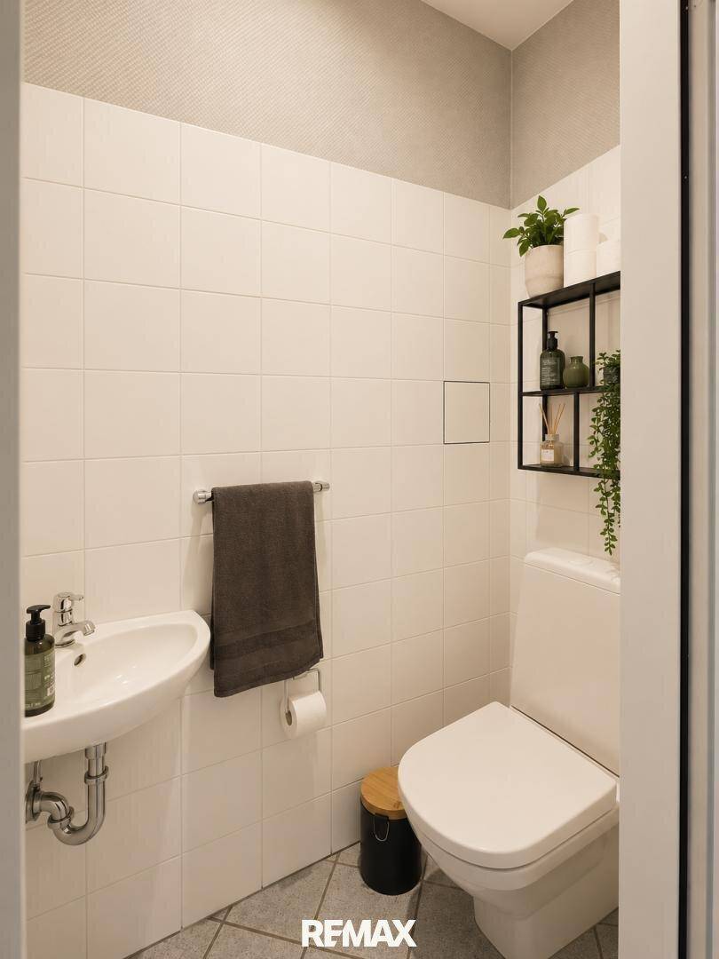 Kleines Gäste-WC mit weißen Fliesen, wandmontierter Toilette und einem Waschbecken.