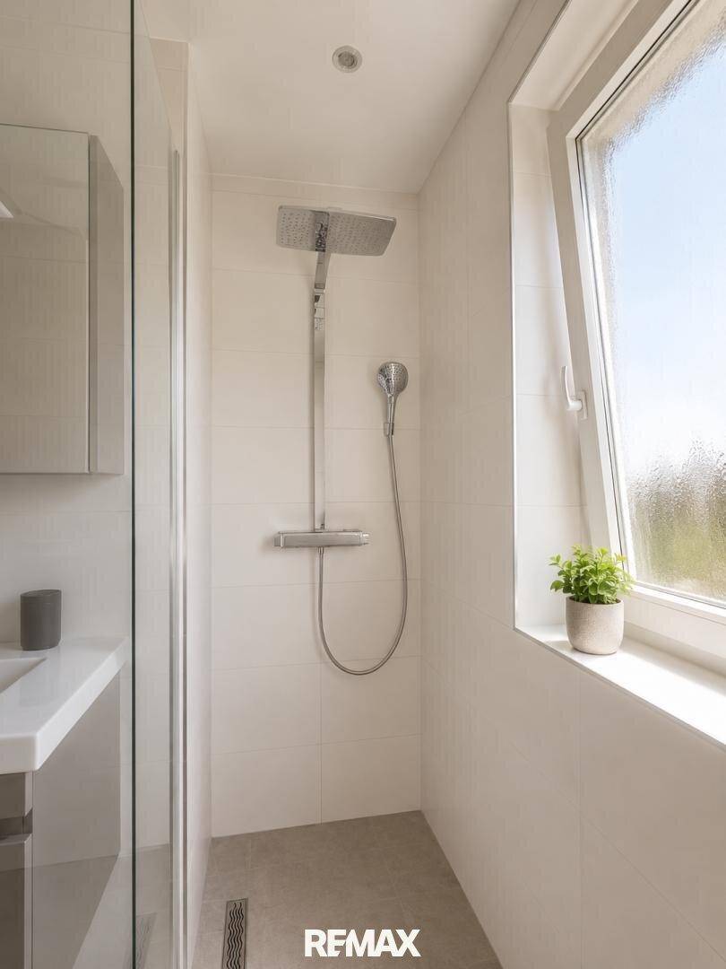 Modernes Badezimmer mit ebenerdiger Dusche, weißen Fliesen und einem Fenster für Tageslicht.
