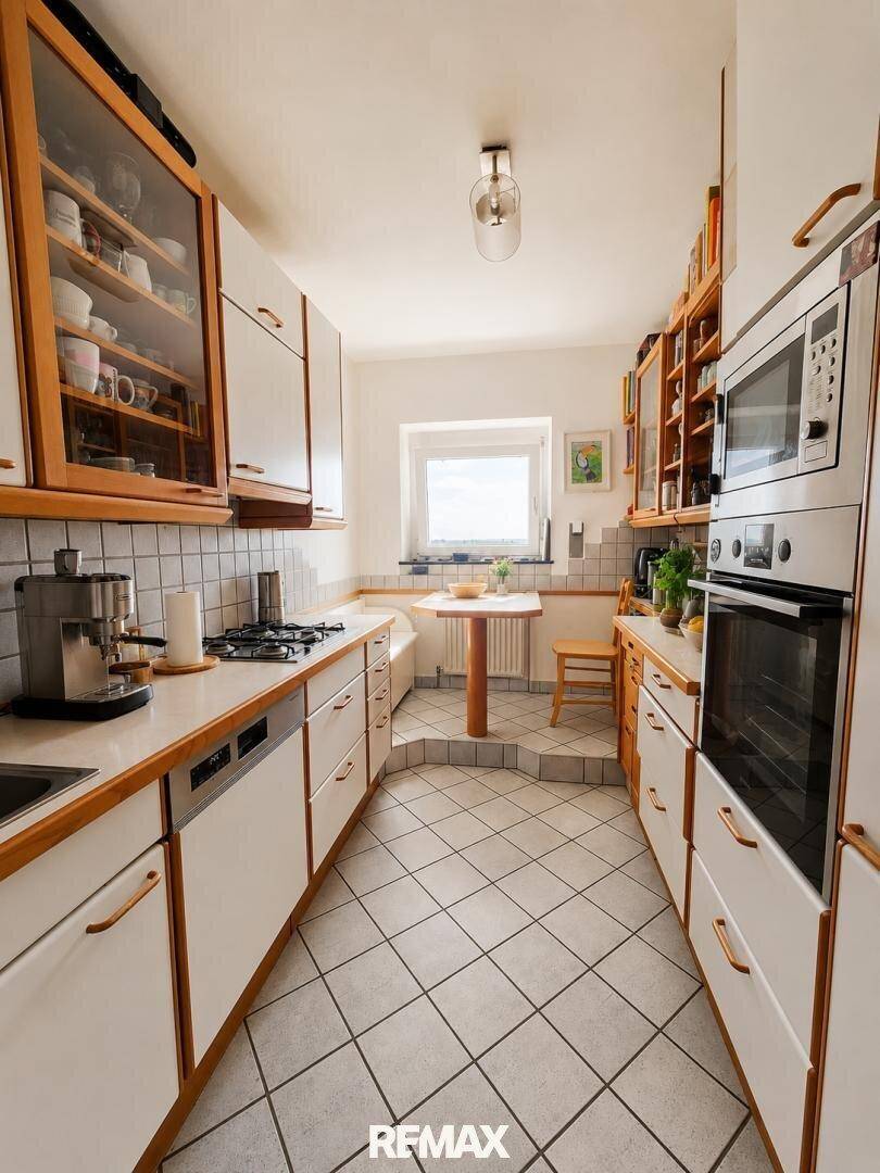 Funktionale Küche mit weißen Schränken, Holzarbeitsplatten und einem kleinen Essbereich am Fenster.