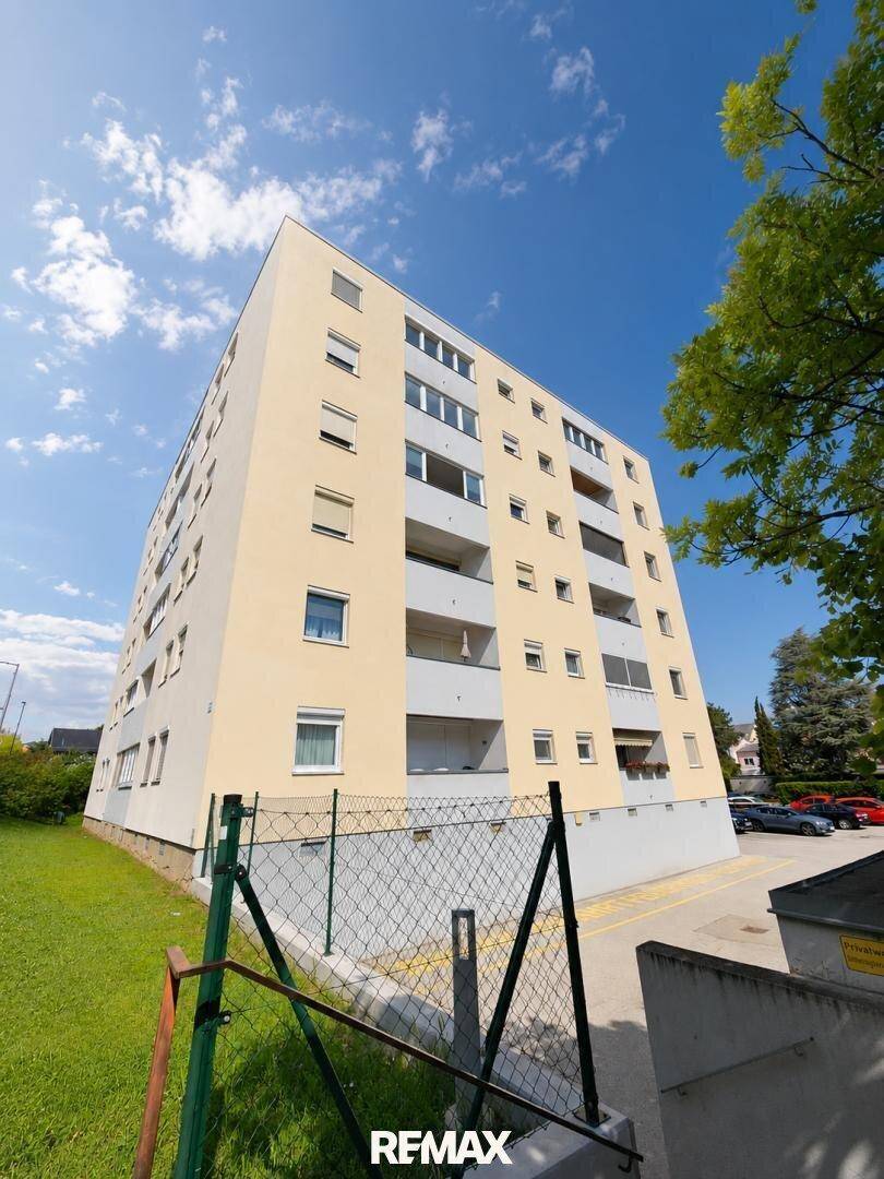 Mehrstöckiges Apartmentgebäude mit gelber Fassade und mehreren Balkonen unter blauem Himmel.