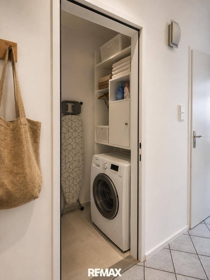 Praktischer Abstellraum mit Waschmaschine, Bügelbrett und Regalen für zusätzlichen Stauraum.