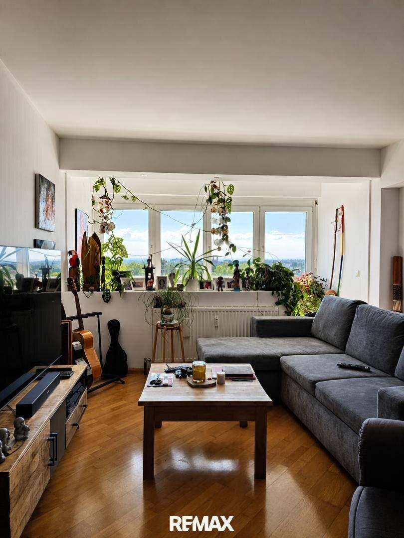 Gemütliches Wohnzimmer mit großem Sofa, Holzboden und Fenstern mit Blick ins Grüne.