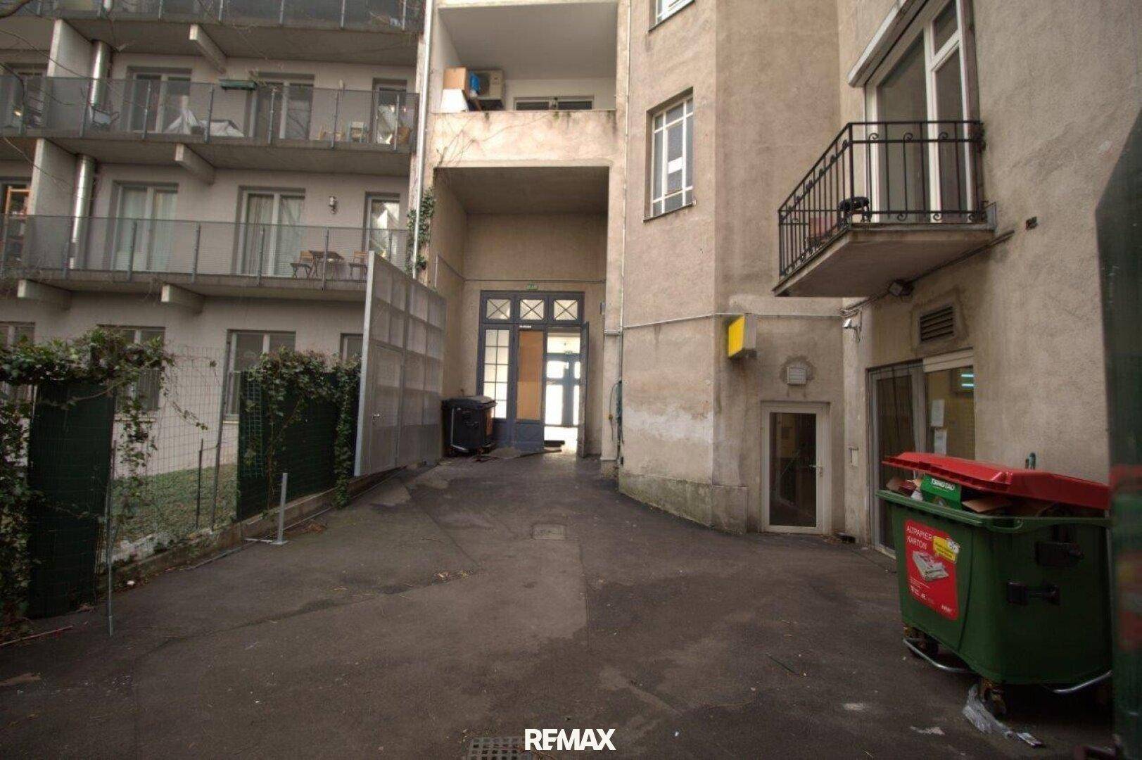 Hinterhofbereich zwischen Gebäuden mit Zugang zu Eingängen und Mülltonnen.
