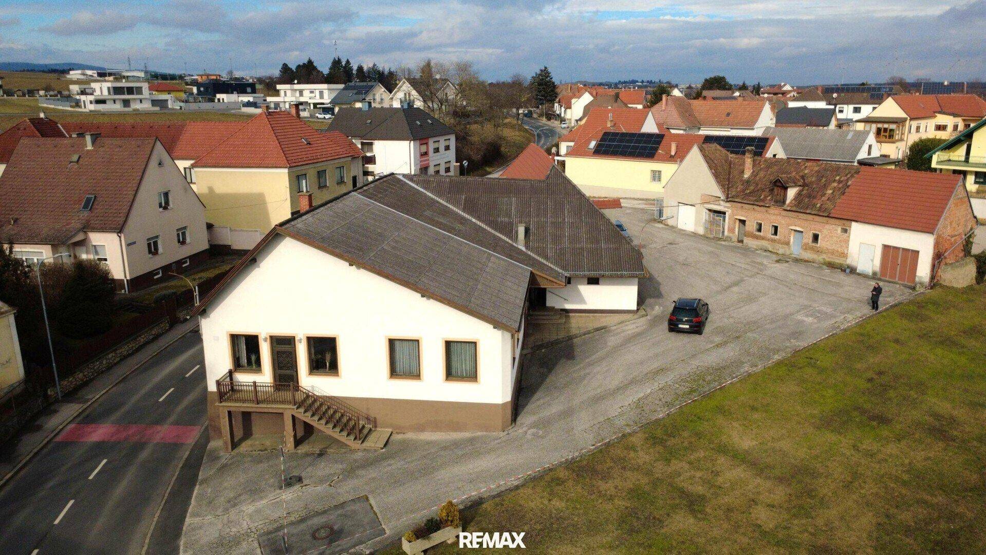 Panoramische Luftansicht eines Gebäudekomplexes mit angrenzenden Feldern und Wohnbebauung.