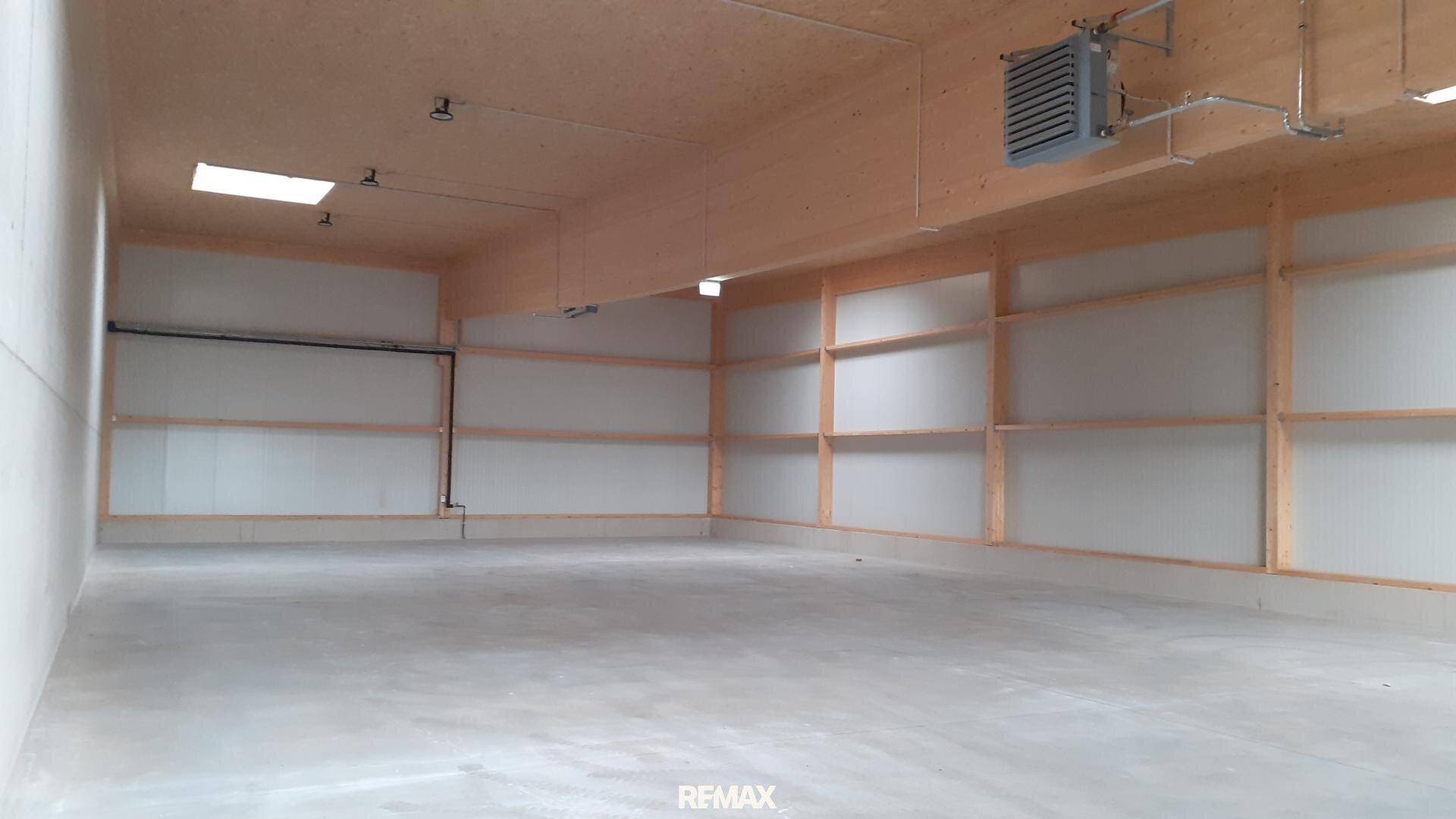 Geräumige, leere Lagerhalle mit hohen Decken, sichtbaren Holzträgern und einem Betonboden, beleuchtet durch Oberlichter.