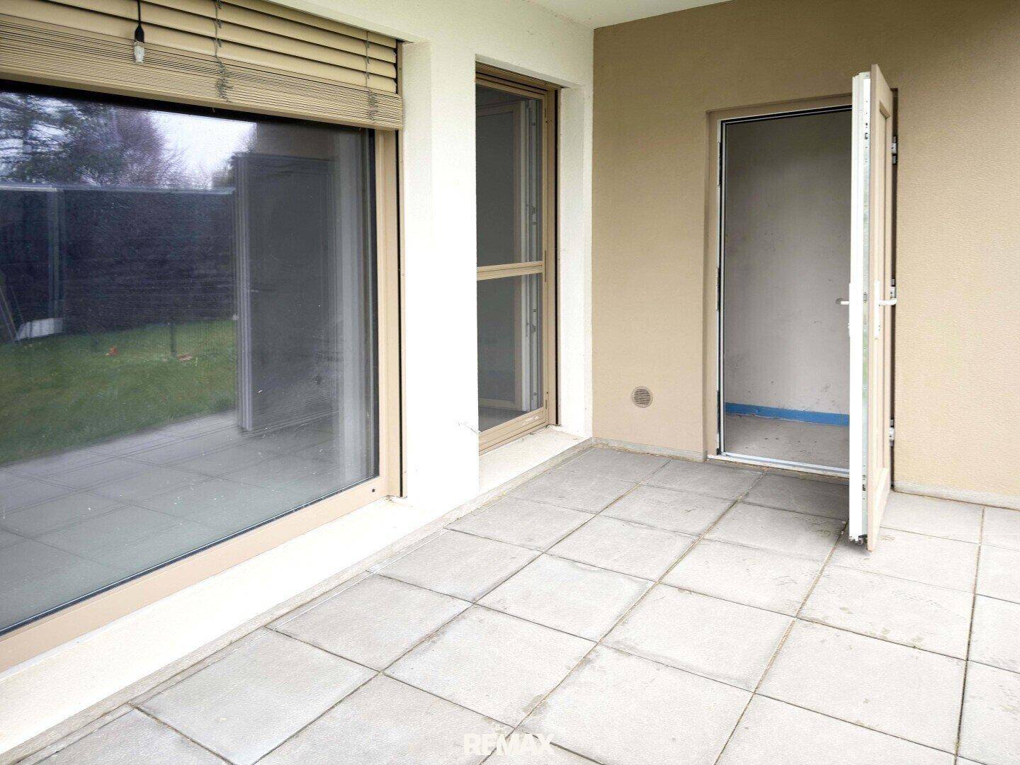 Kleine Terrasse mit Fliesenboden und Zugang zum Garten, bereit für individuelle Gestaltung.