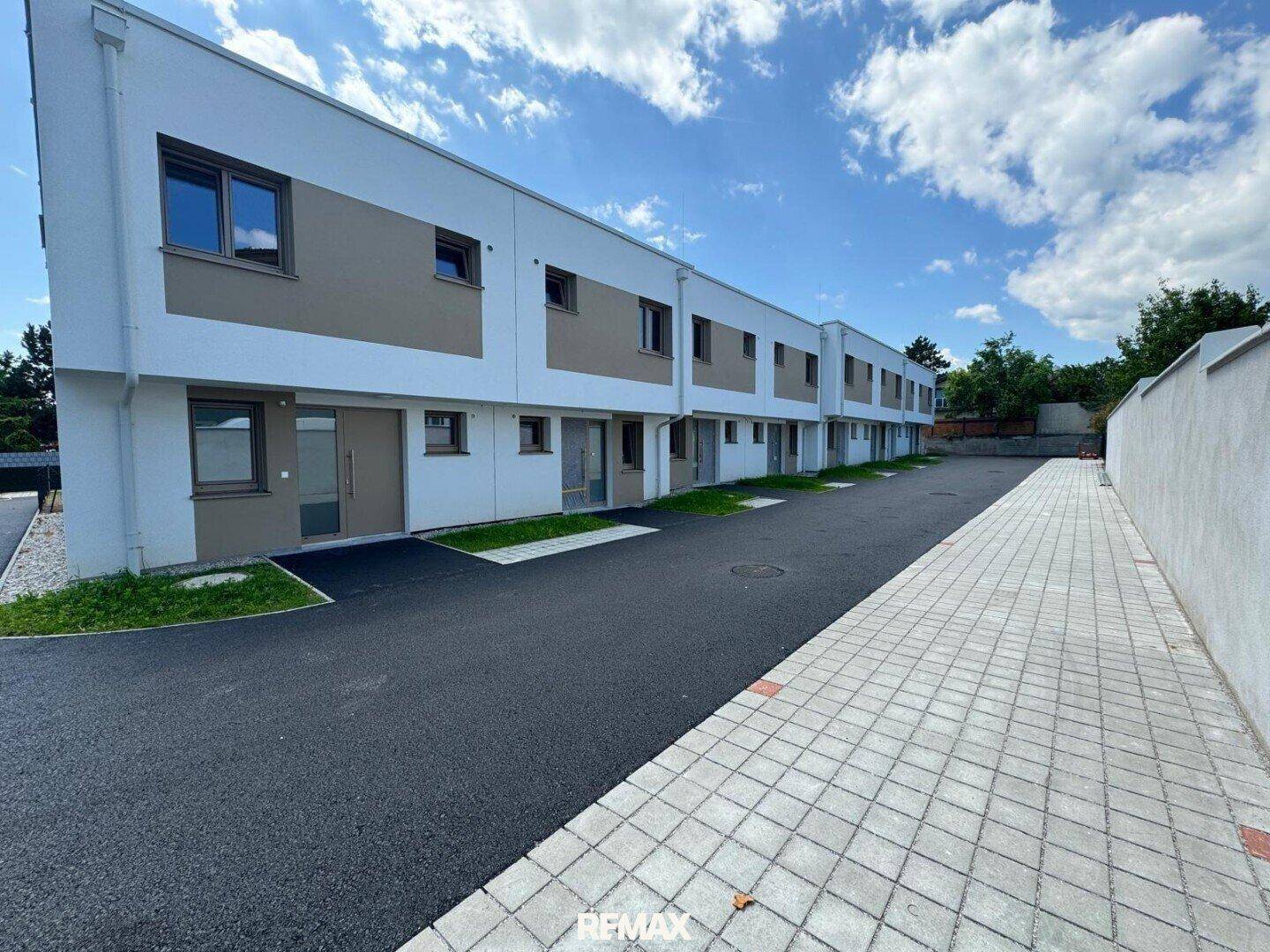 Reihenhäuser mit weißer Fassade und braunen Akzenten in einer ruhigen Wohngegend.