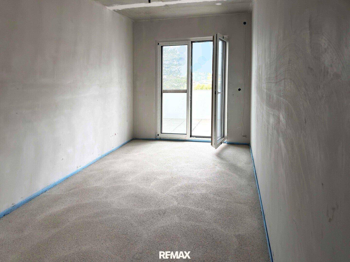 Unfertiges Schlafzimmer im Rohbau mit Estrichboden und Zugang zu einem Balkon oder einer Terrasse.