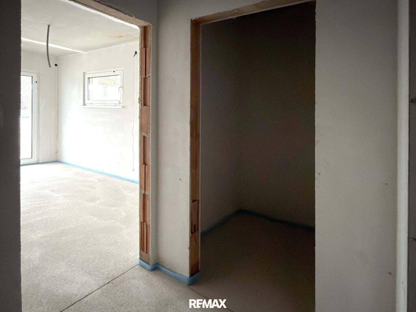 Innenraum im Rohbau mit Türrahmen und Estrichboden, der auf den weiteren Ausbau wartet.
