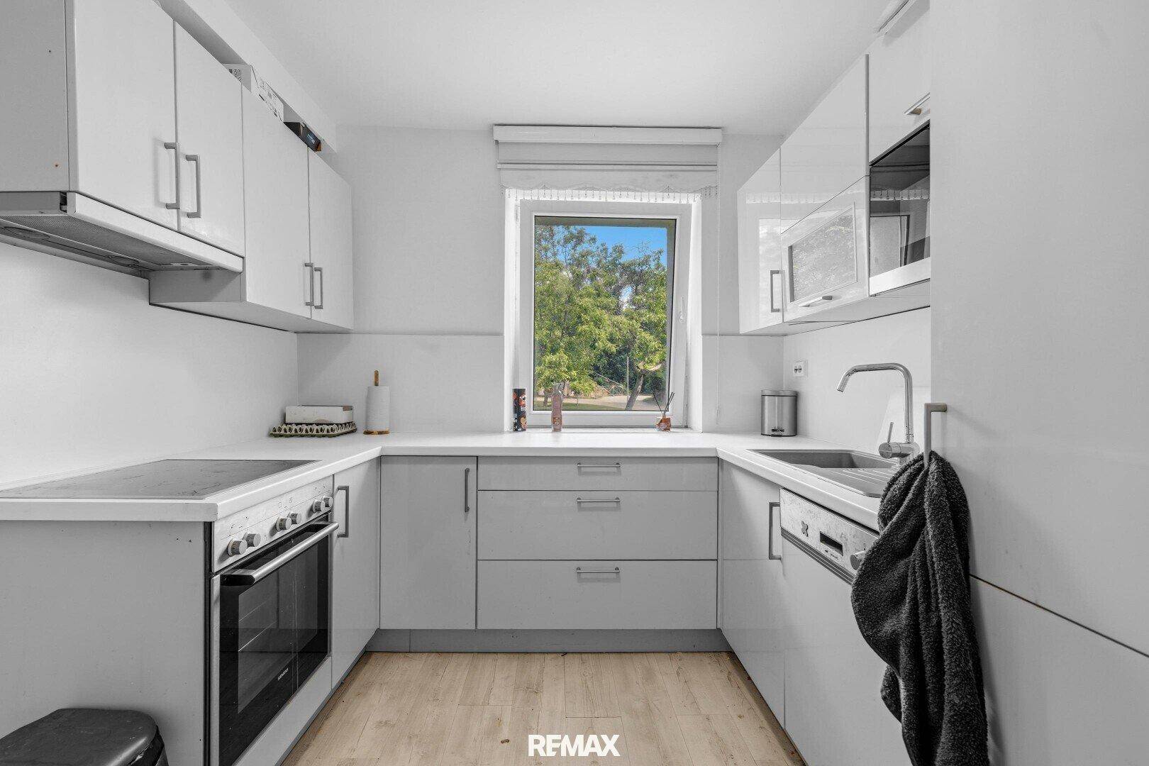 Moderne Küche mit weißen Hochglanzschränken, integrierten Geräten und Fensterblick ins Grüne.