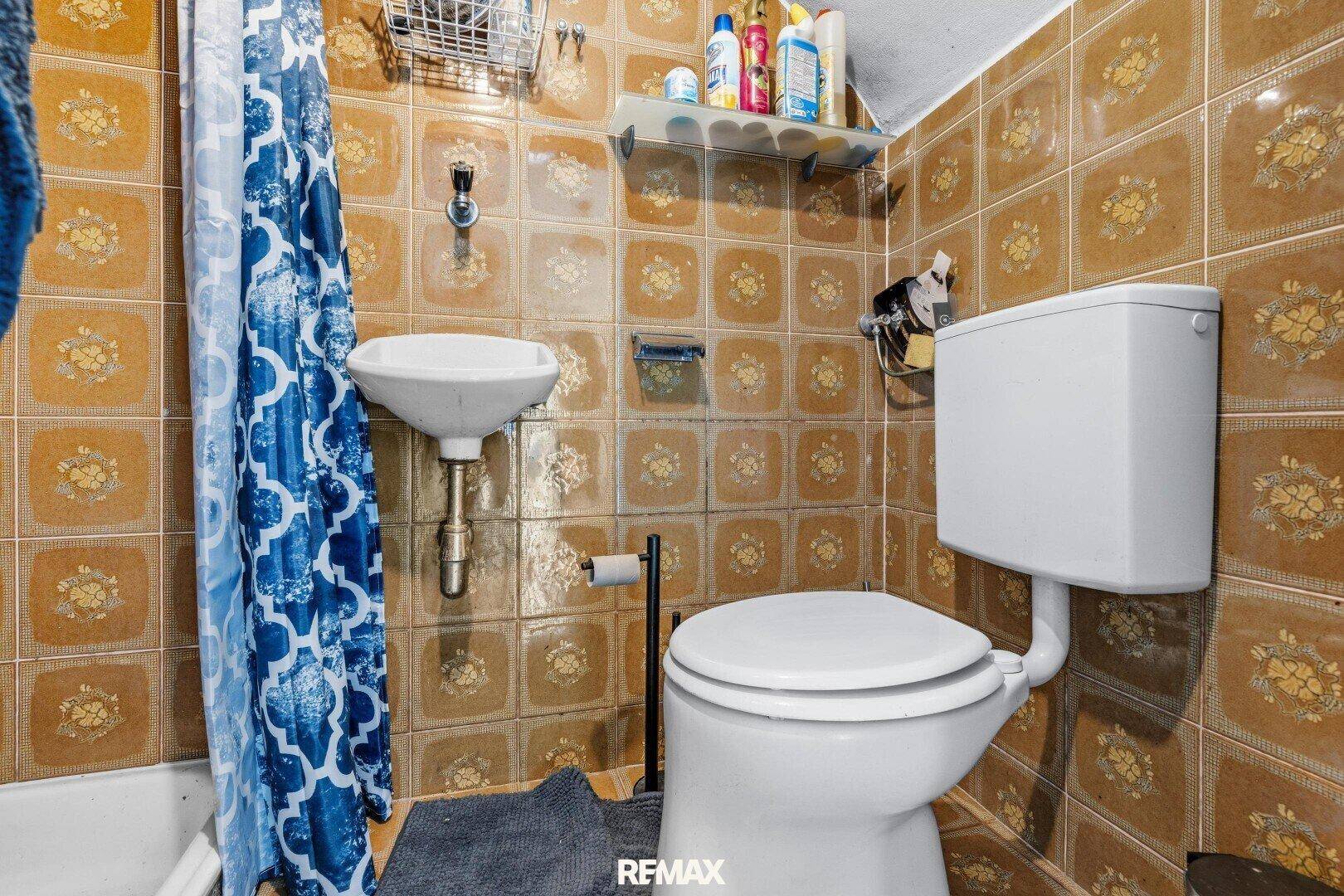 Kleines Badezimmer mit braunen Fliesen, Waschbecken und Toilette im 80er-Jahre-Stil.
