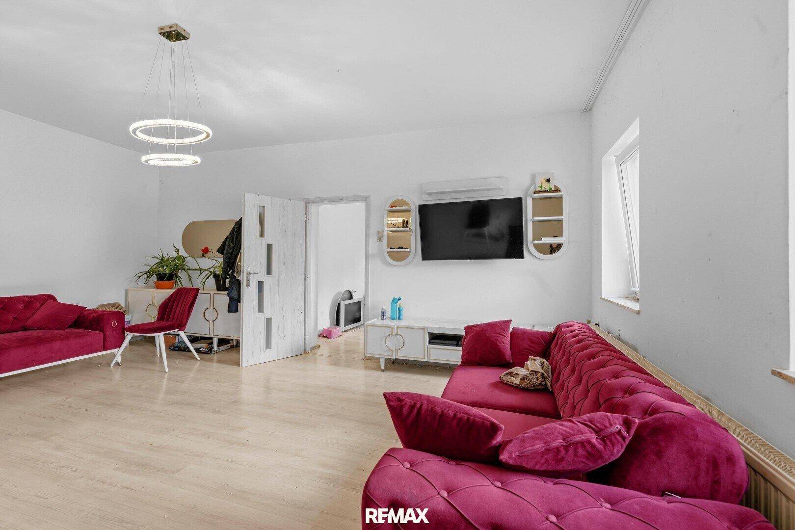 Helles Wohnzimmer mit modernen Deckenleuchten, roten Samtsofas und hellem Laminatboden.
