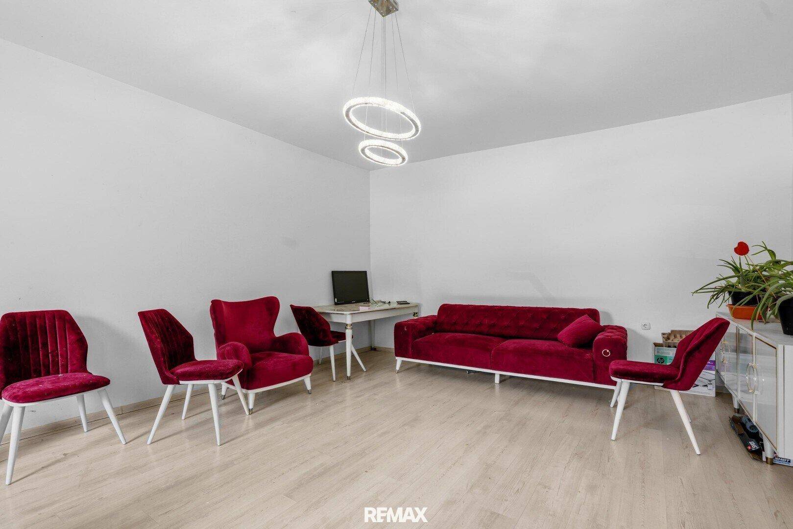 Geräumiges Wohnzimmer mit roter Samtpolsterung, modernem Licht und hellem Laminatboden.