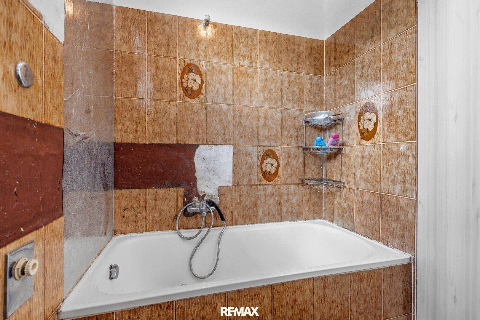Badezimmer mit braunen Fliesen und Badewanne, renovierungsbedürftig und funktional.