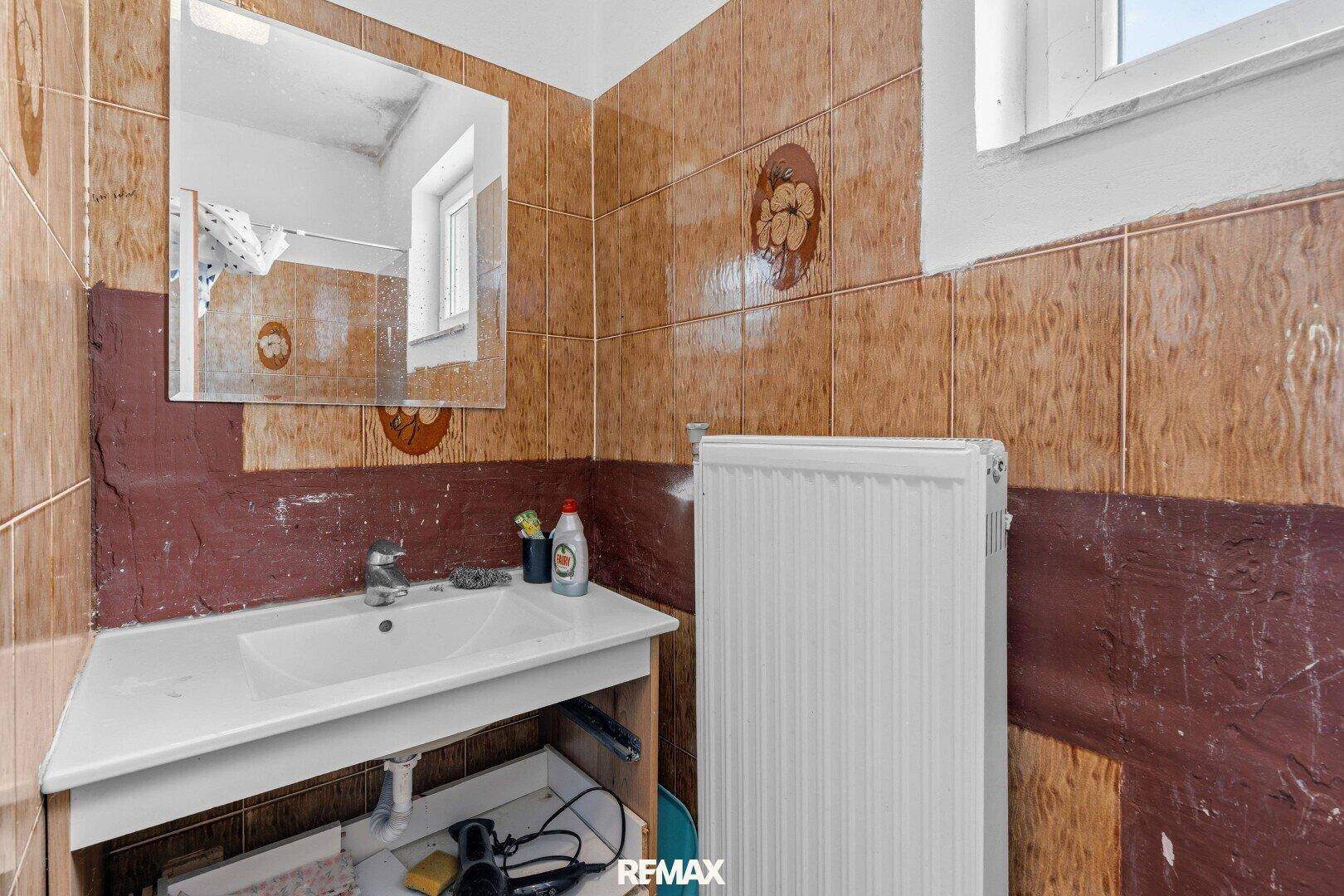 Badezimmer mit braunen Fliesen, Waschbecken und Heizkörper, renovierungsbedürftig.