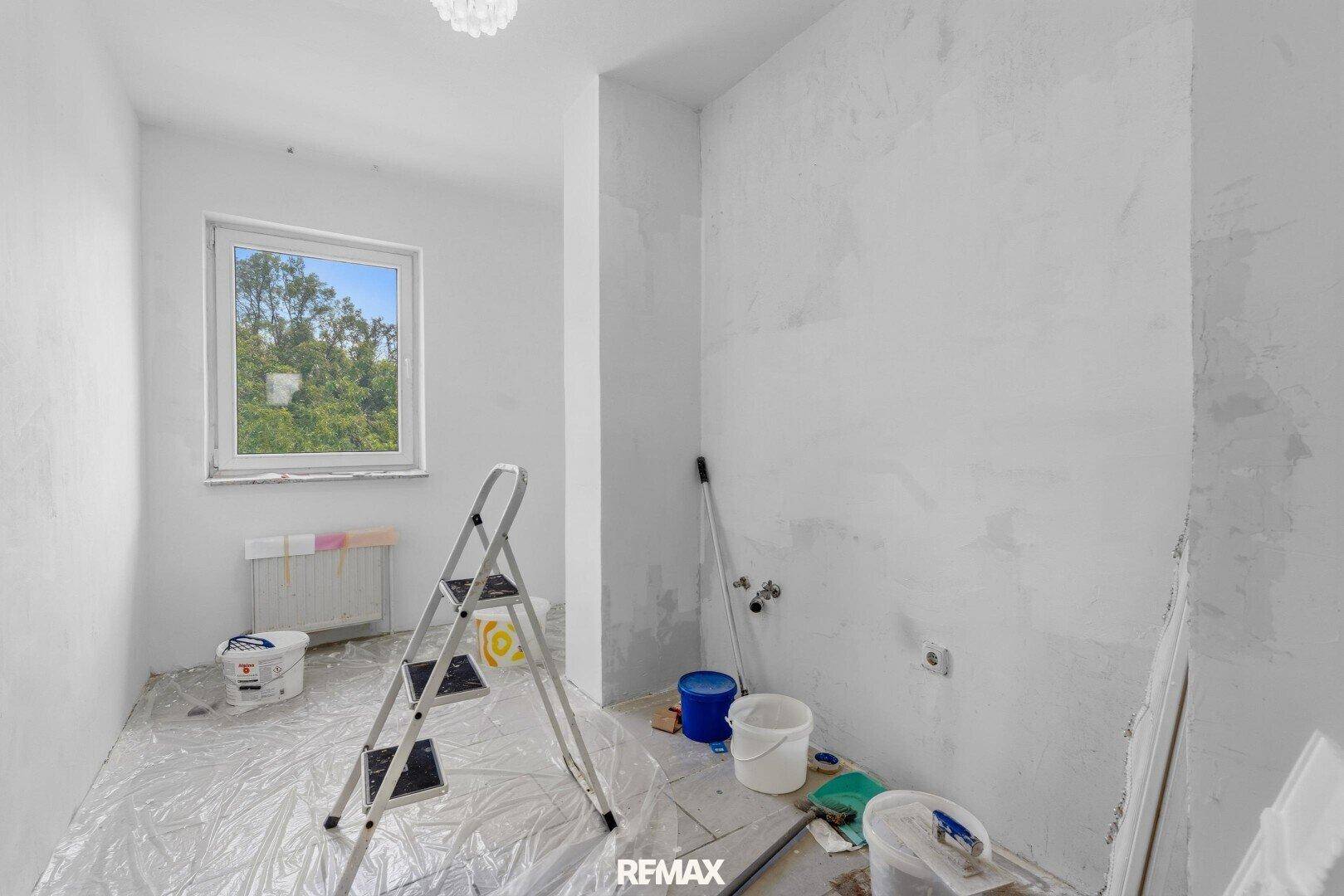 Raum in Renovierung mit Leiter, Farbeimern und Fenster, bereit für die Fertigstellung.