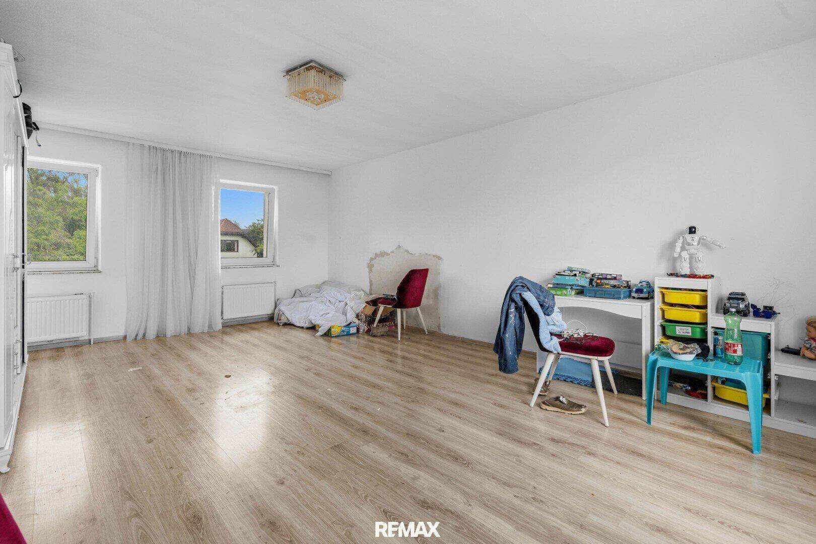 Kinderzimmer mit hellem Laminatboden, zwei Fenstern und viel Platz zum Spielen.