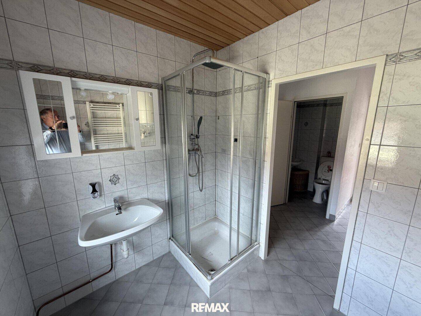 Gefliestes Badezimmer mit Eckdusche, Waschbecken und Holzdecke.