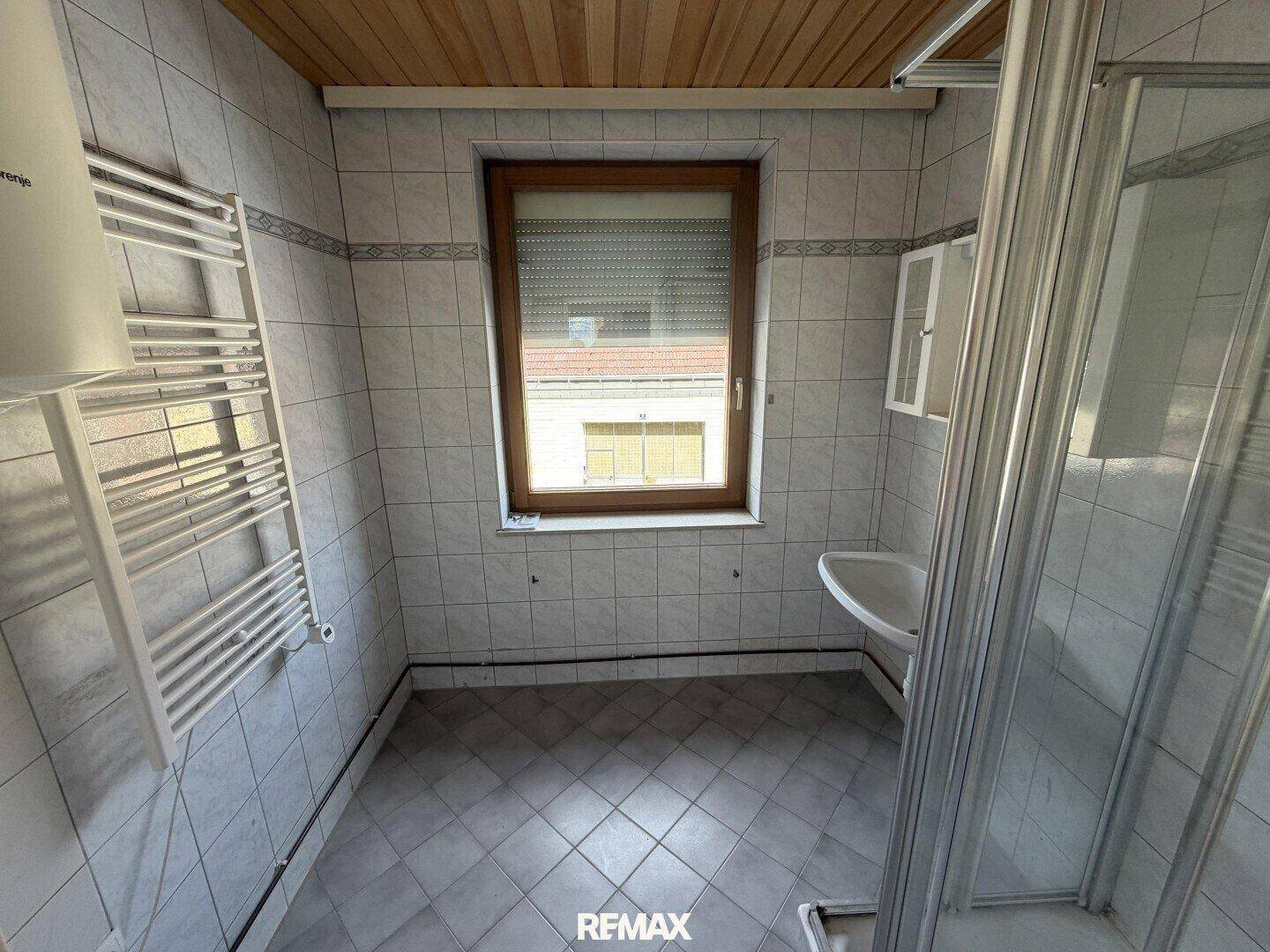 Badezimmer mit Fliesen, Fenster, beheiztem Handtuchhalter und Holzdecke.
