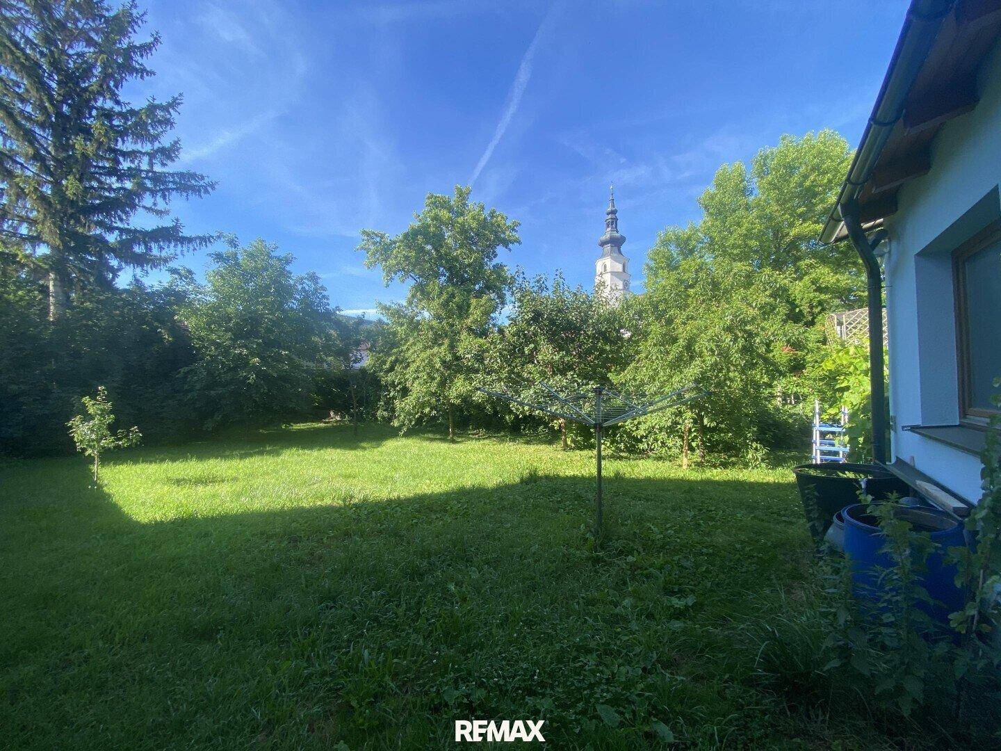 Großer grüner Garten mit Bäumen und Blick auf einen Kirchturm.