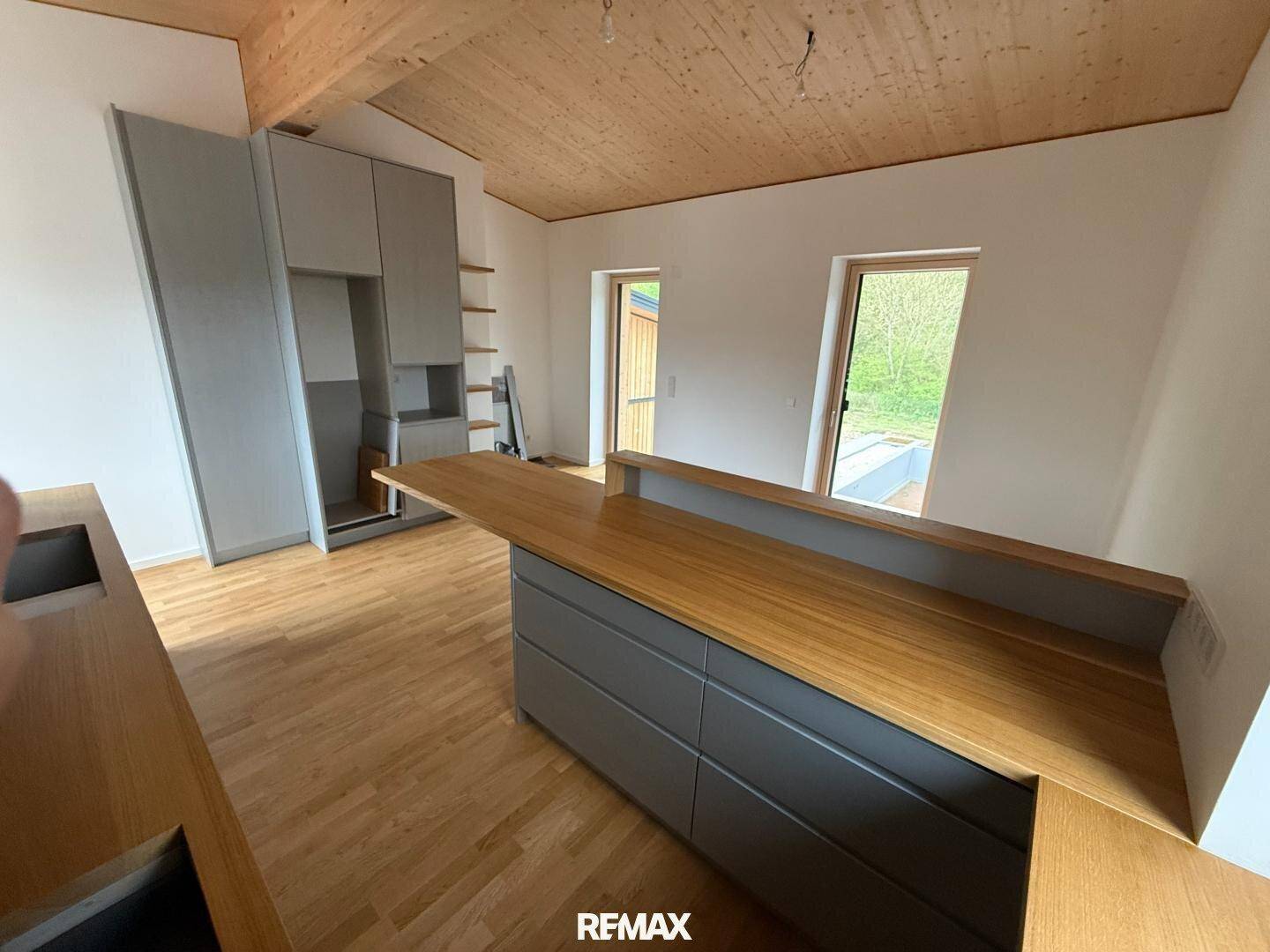 Helle Küche mit Holztheke, grauen Schränken und Zugang zum Außenbereich.