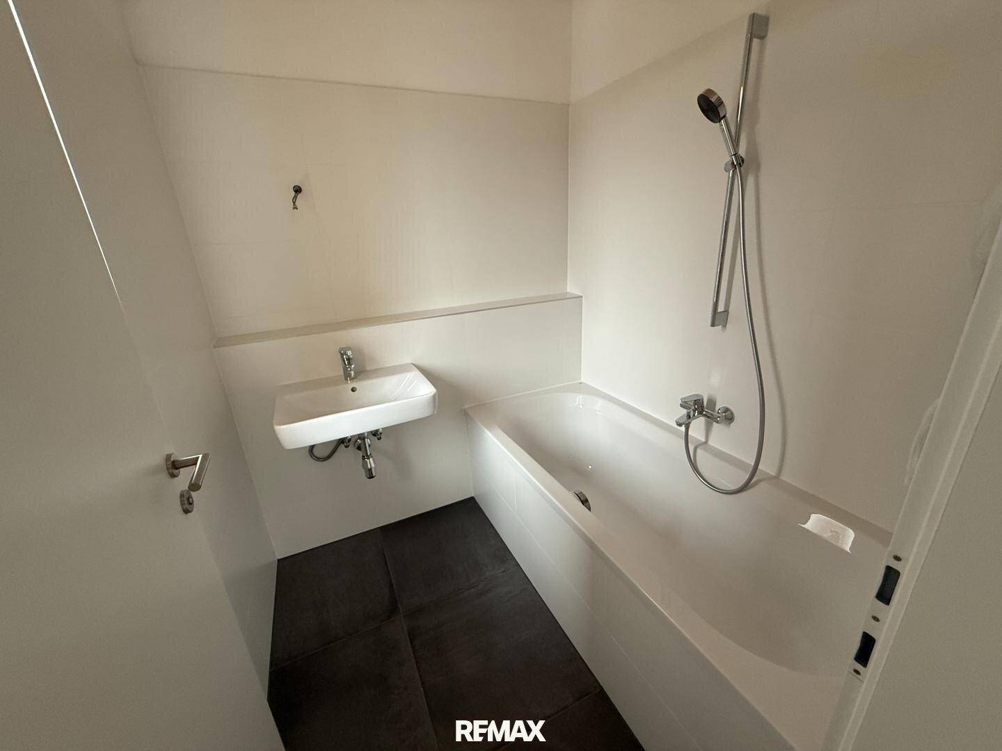Helles Badezimmer mit Badewanne, Waschbecken und Duscharmatur.