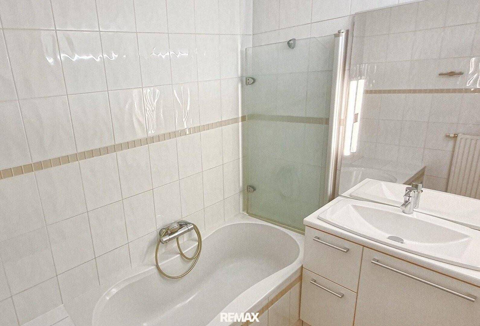 Badezimmer mit Badewanne, Duschabtrennung und Waschbecken, komplett gefliest.