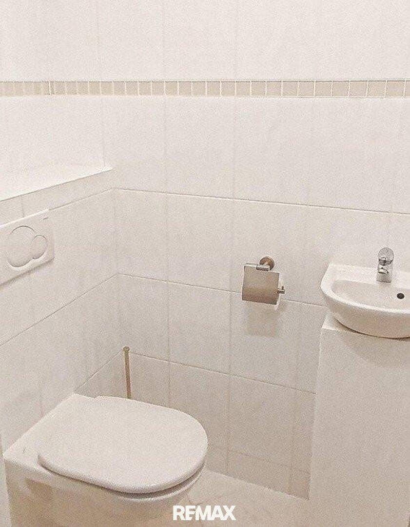 Kleines Gäste-WC mit Toilette und Handwaschbecken, hell gefliest.