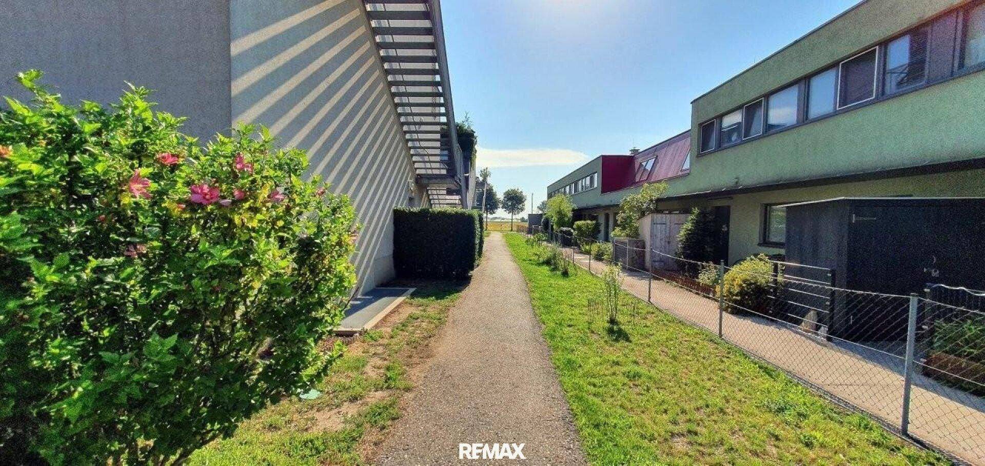 Fußweg zwischen Reihenhäusern mit gepflegten Grünflächen und Hecken.