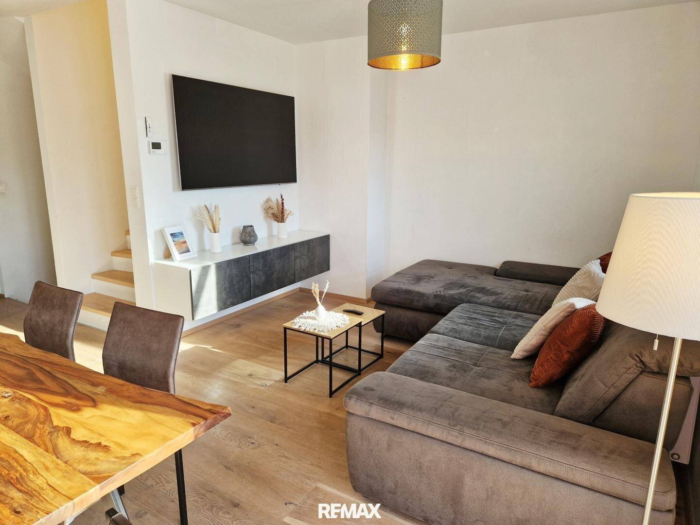 Wohnzimmer mit großem Sofa, Wandfernseher und Holzboden, offen zum Essbereich.