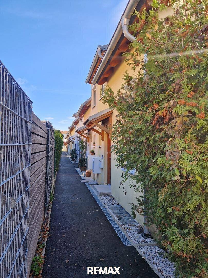 Seitlicher Zugangsweg zwischen den Häusern mit Gabionenzaun und grüner Bepflanzung.