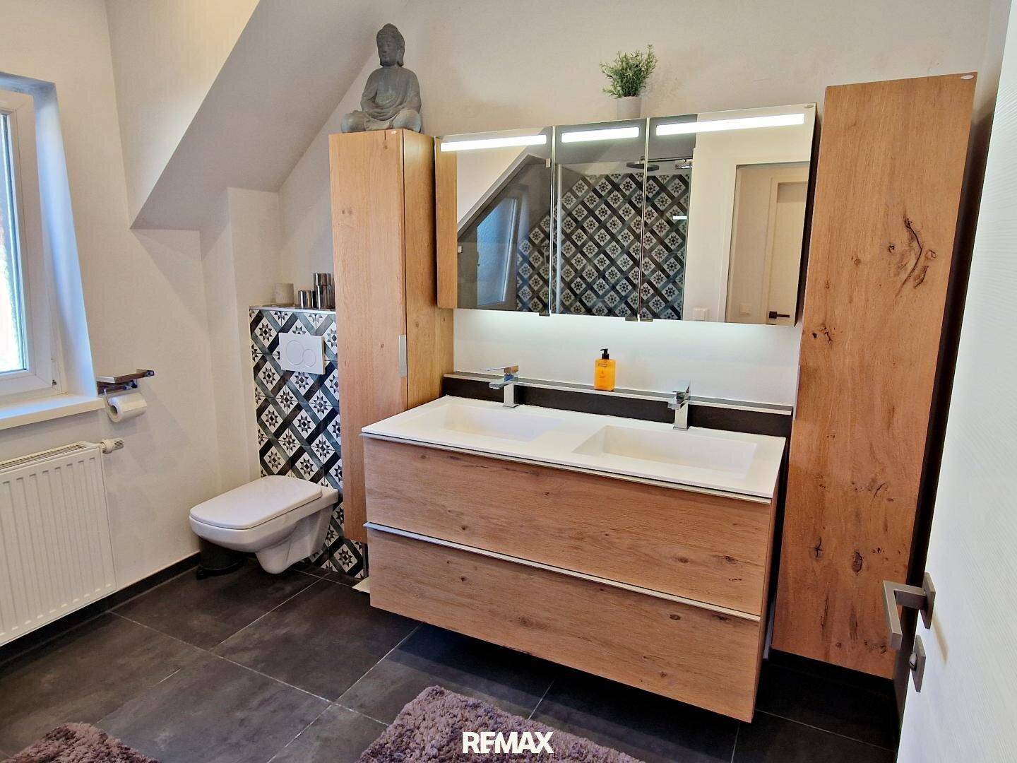 Modernes Badezimmer mit Doppelwaschbecken, Holzmöbeln und gemusterten Fliesen.