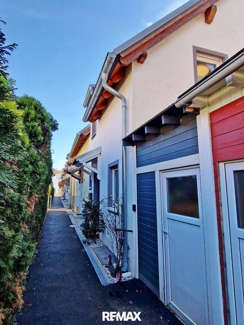Schmaler Zugangsweg zwischen den Häusern mit gepflegter Hecke und blauer Fassade.