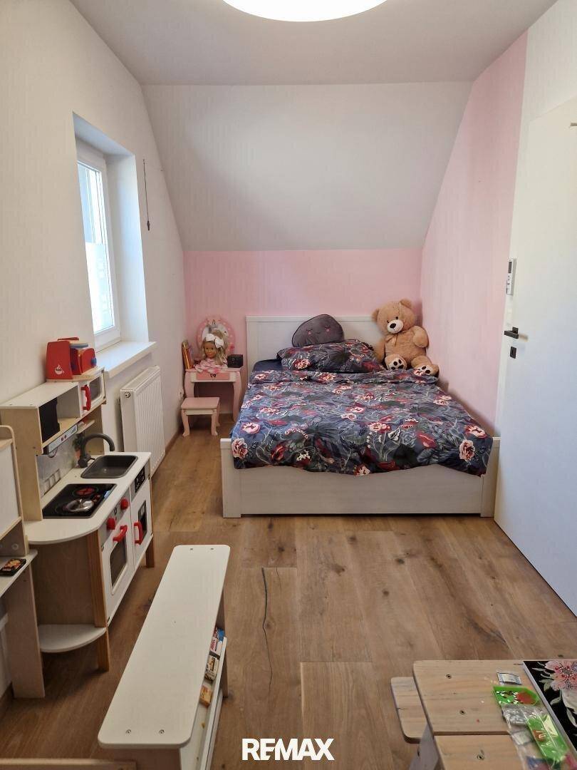 Kinderzimmer mit Bett, Spielküche und Holzboden, hell und freundlich gestaltet.