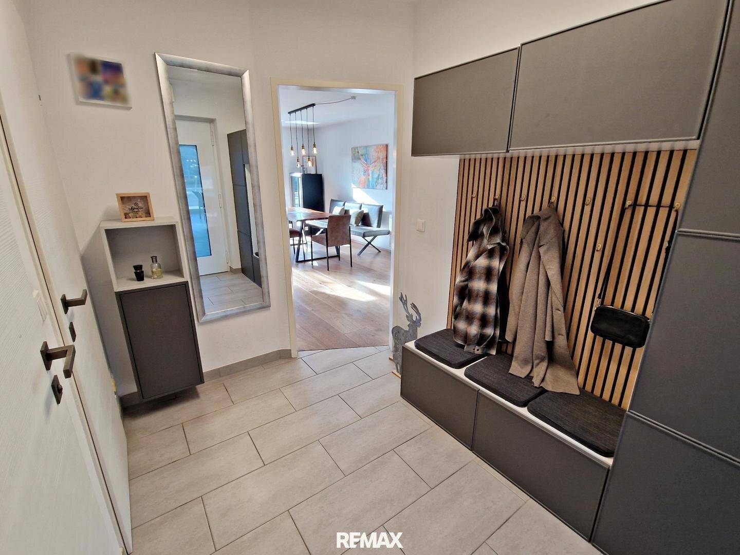 Moderner Eingangsbereich mit Fliesenboden, Garderobe und Spiegel, offen zum Wohnbereich.