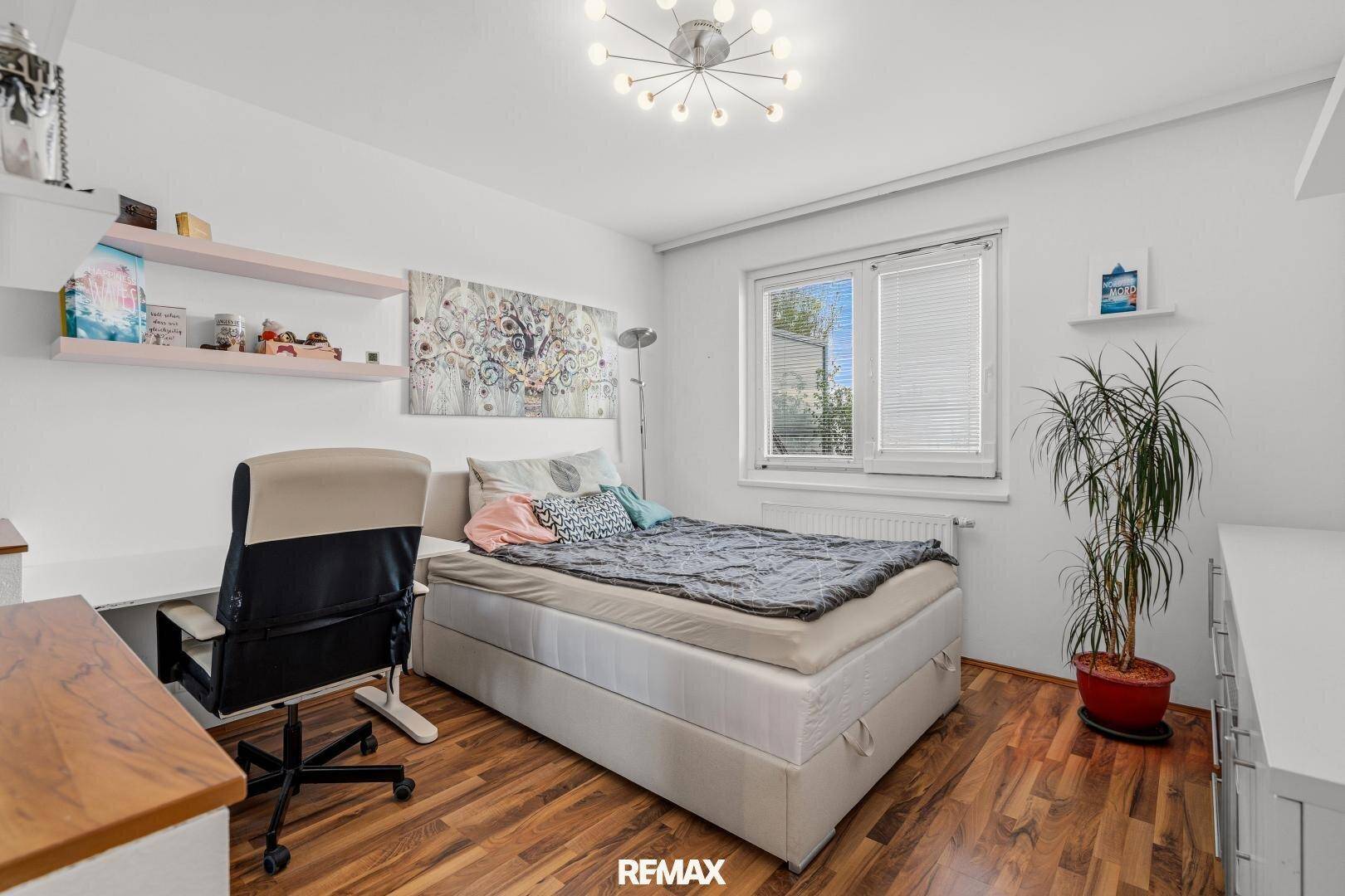 Geräumiges Schlafzimmer mit Bett, Schreibtisch und Zimmerpflanze, mit Holzboden.