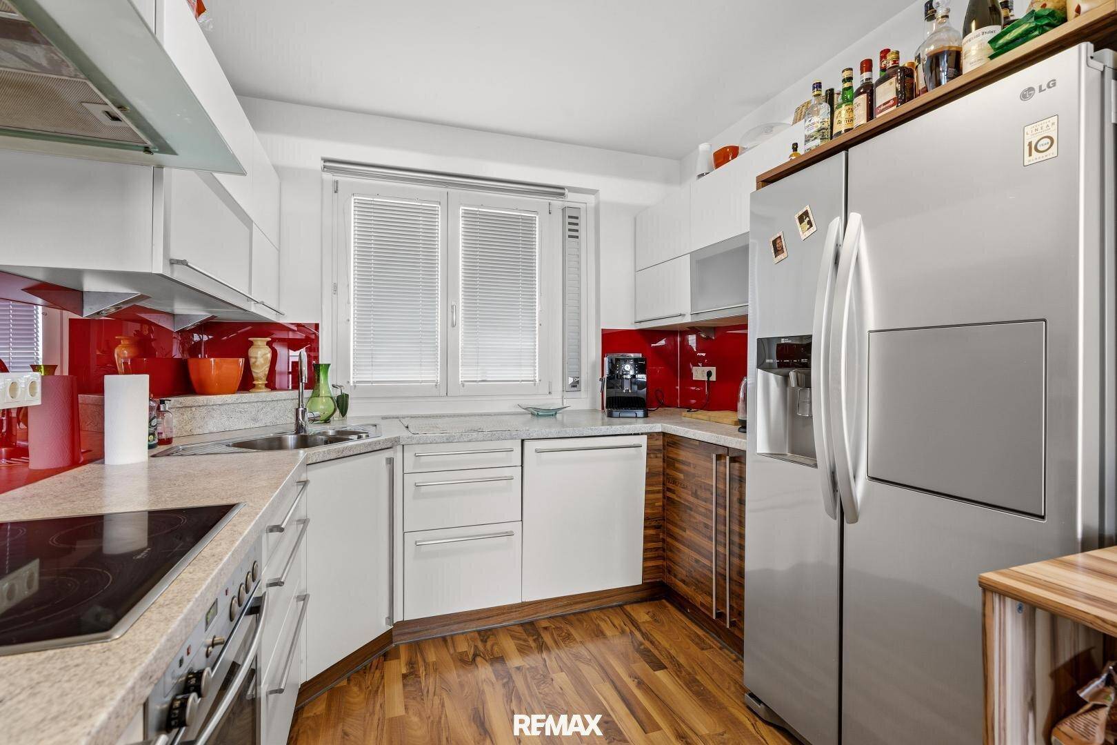 Funktionale Küche mit weißen und holzfarbenen Schränken, roter Rückwand und großem Kühlschrank.