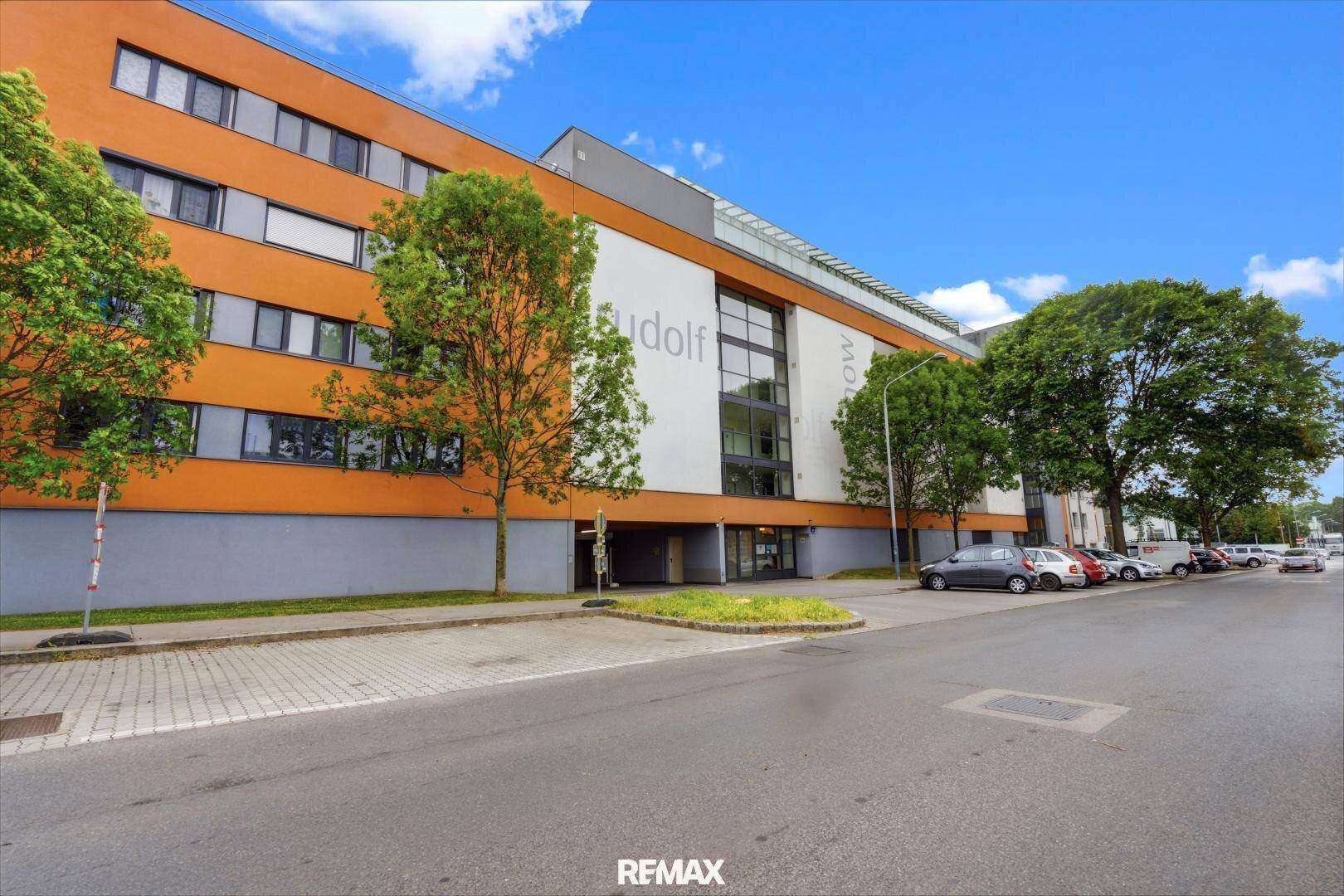 Moderne Gebäudefassade mit orangefarbenen und weißen Akzenten an einer Straße.