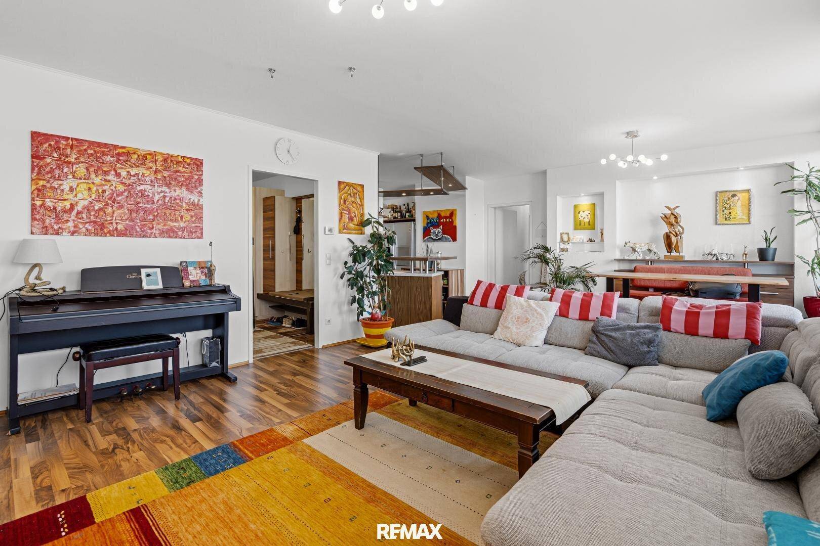 Geräumiges Wohnzimmer mit großem Sofa, Klavier und farbenfrohem Teppich, offen gestaltet.
