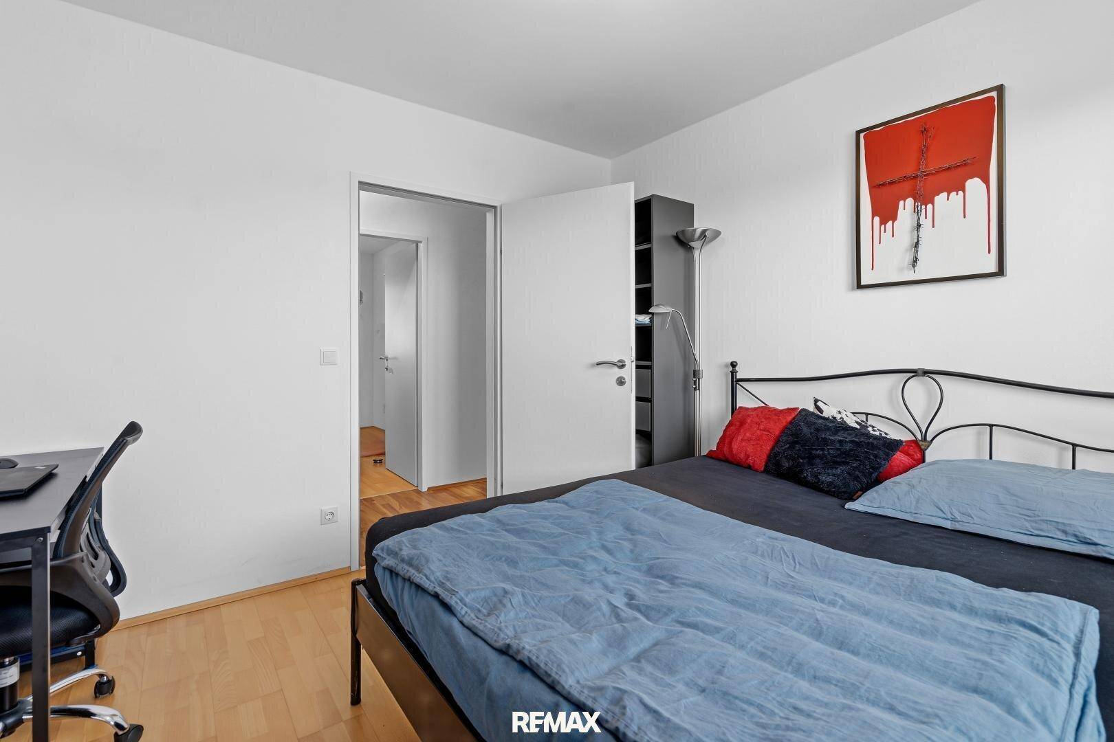 Schlafzimmer mit Bett und Schreibtisch, schlicht eingerichtet und hell.