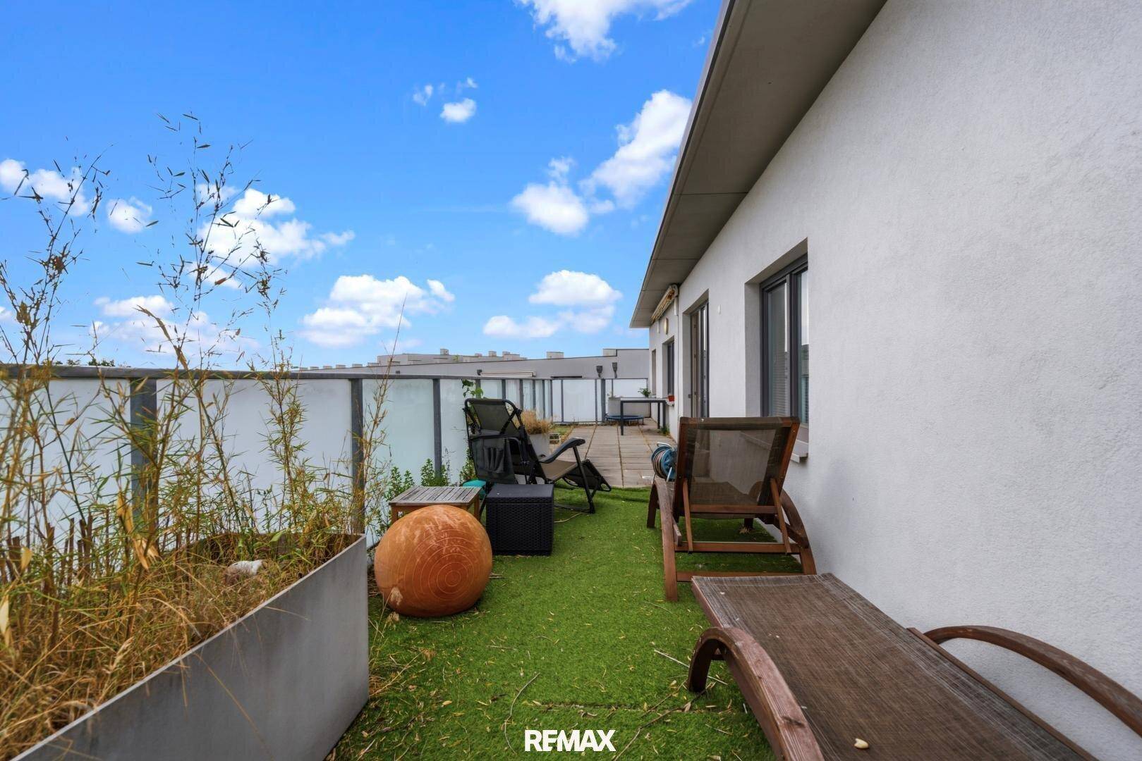 Gemütliche Terrasse mit Kunstrasen, Liegestühlen und Pflanzen, ideal zum Entspannen.