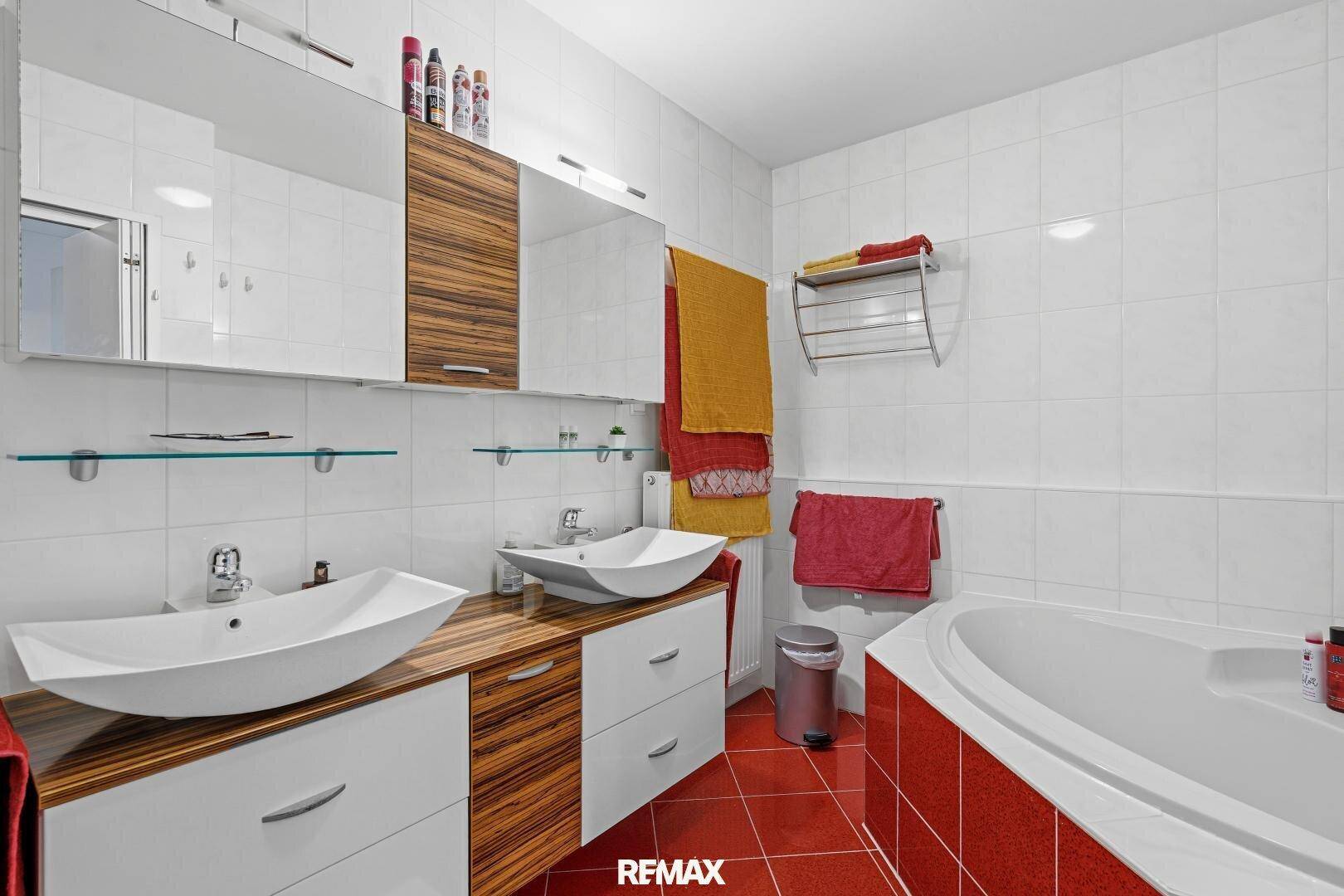 Modernes Badezimmer mit Doppelwaschbecken, Badewanne und roten Bodenfliesen.