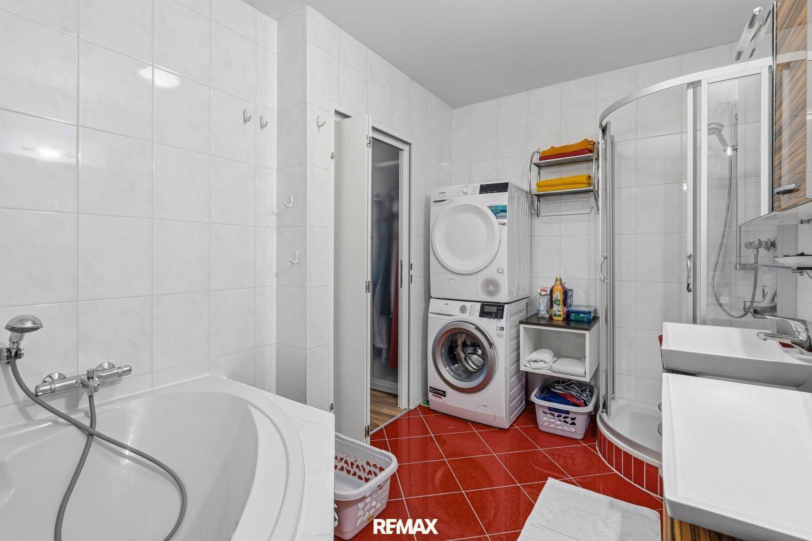 Badezimmer mit Badewanne, Dusche und Waschmaschine/Trockner, rote Bodenfliesen.
