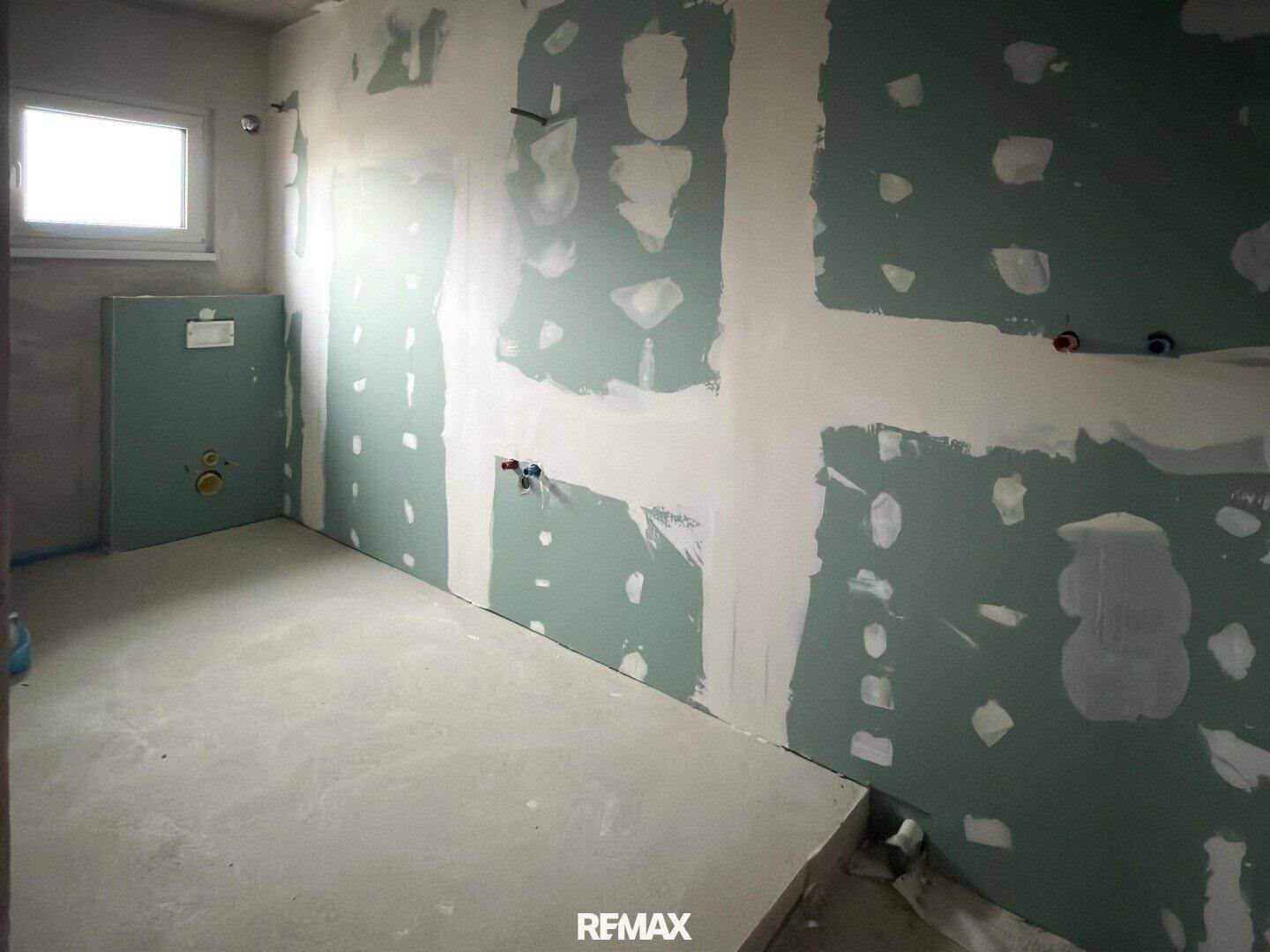 Unfertiges Badezimmer mit Trockenbauwänden und Fenster, vorbereitet für die Installation.
