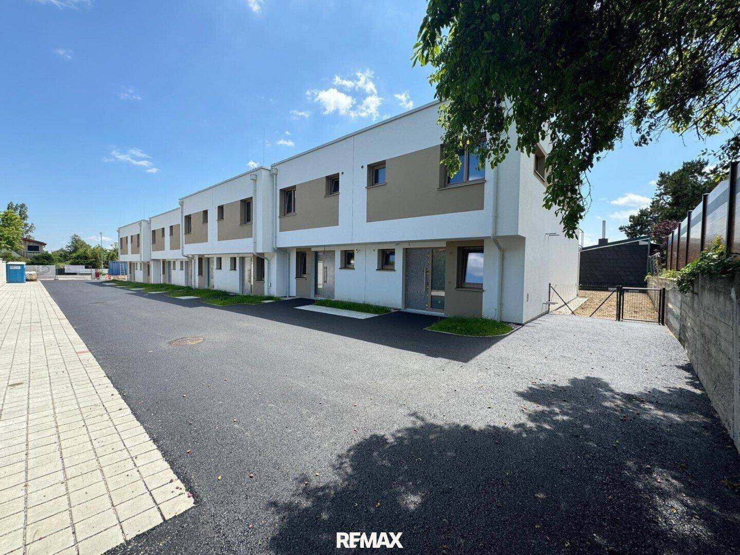 Moderne Reihenhäuser mit weißer und beiger Fassade, umgeben von Grünflächen und Zufahrtswegen.