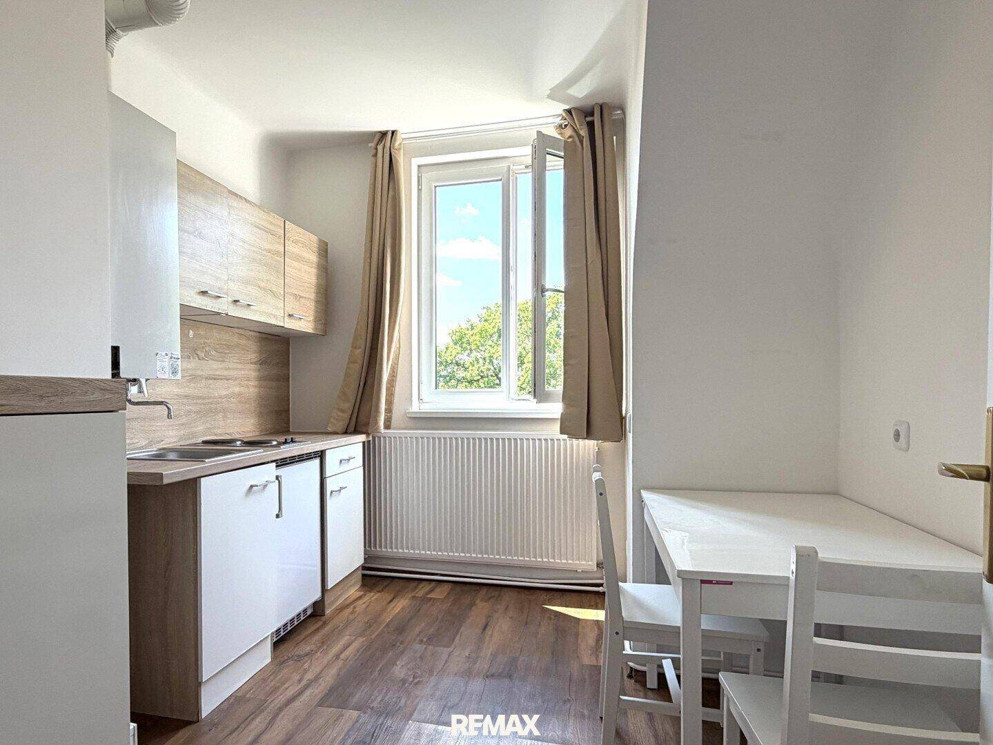 Kleine Küche mit Einbauschränken, Essbereich und Fenster mit Blick ins Grüne.